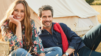 A woman and a man sitting in front of a bell tent wearing clothing from Cotton Traders